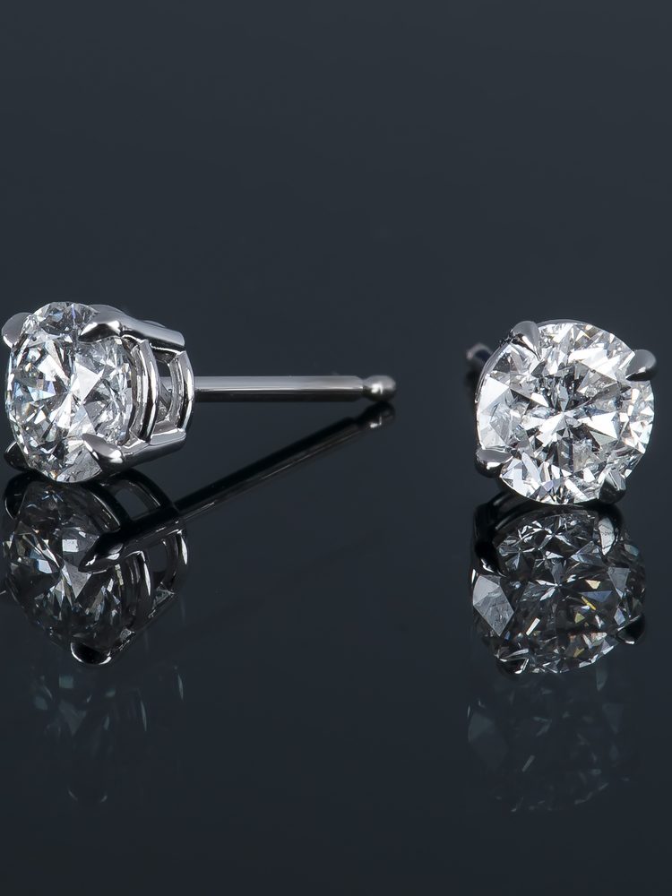 Diamond Stud Earrings Two sparkling diamond stud earrings set in silver, reflecting light on a dark surface.